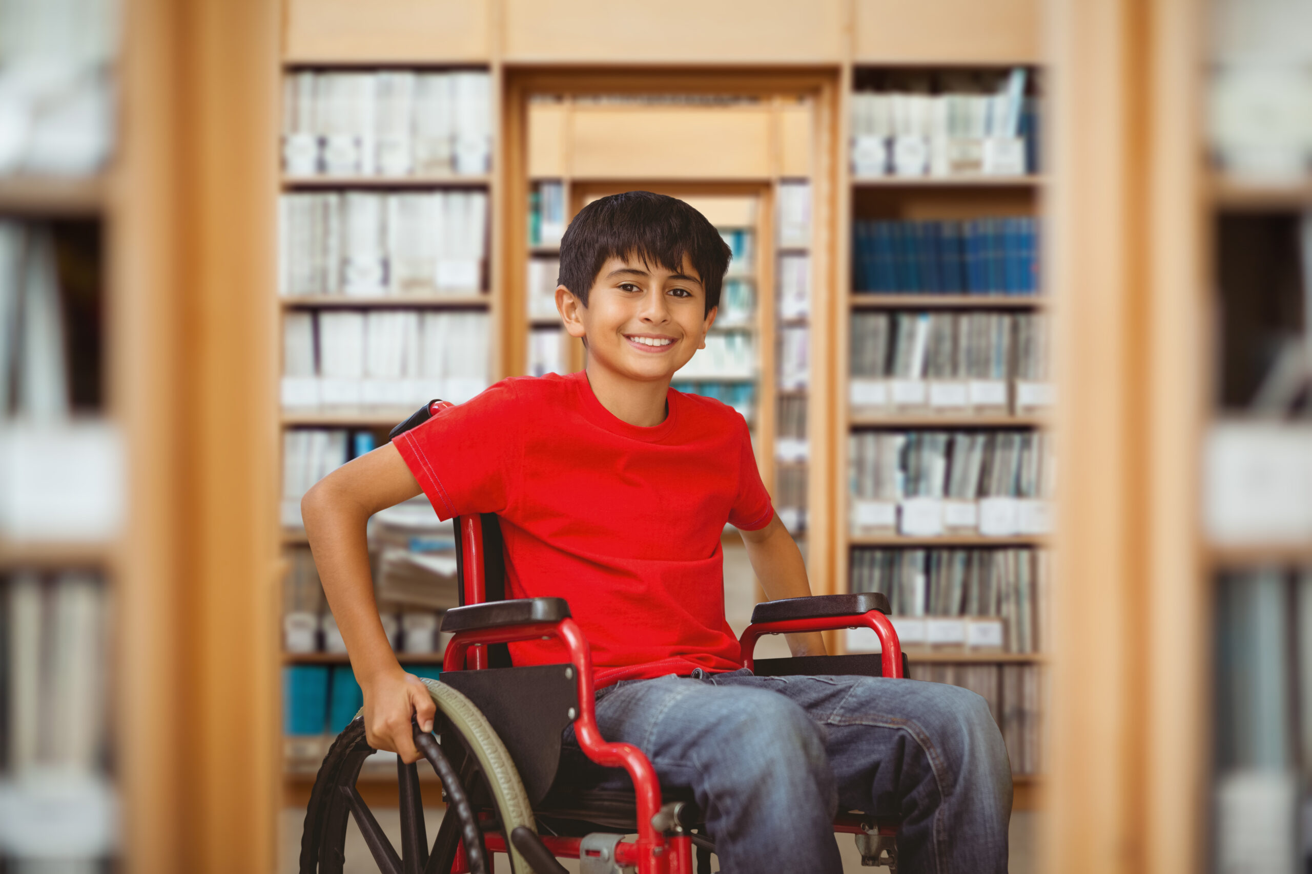 Portrait of boy sitting in wheelchair against library