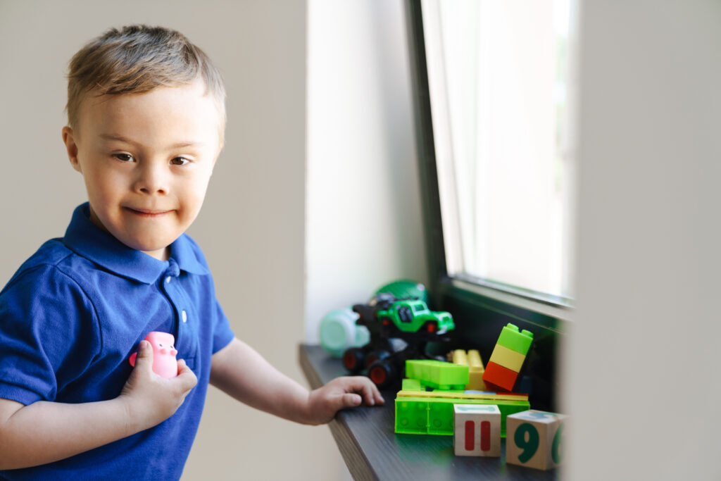 White boy with down syndrome playing with toys by window indoors