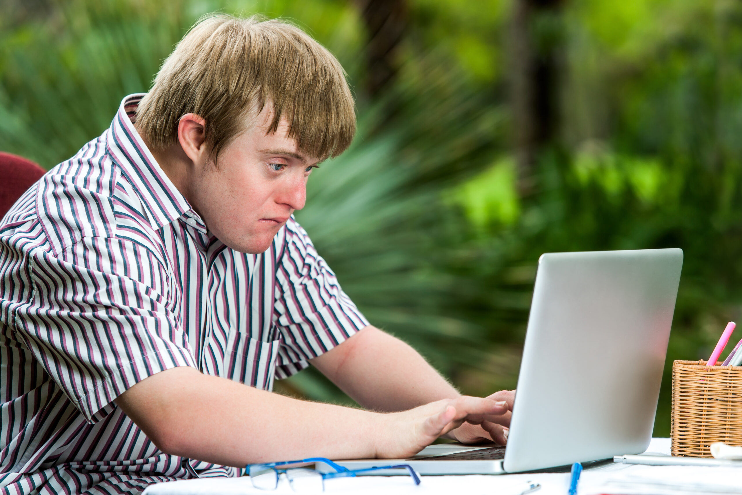 Portrait of concentrated young man with down syndrome working on laptop outdoors.