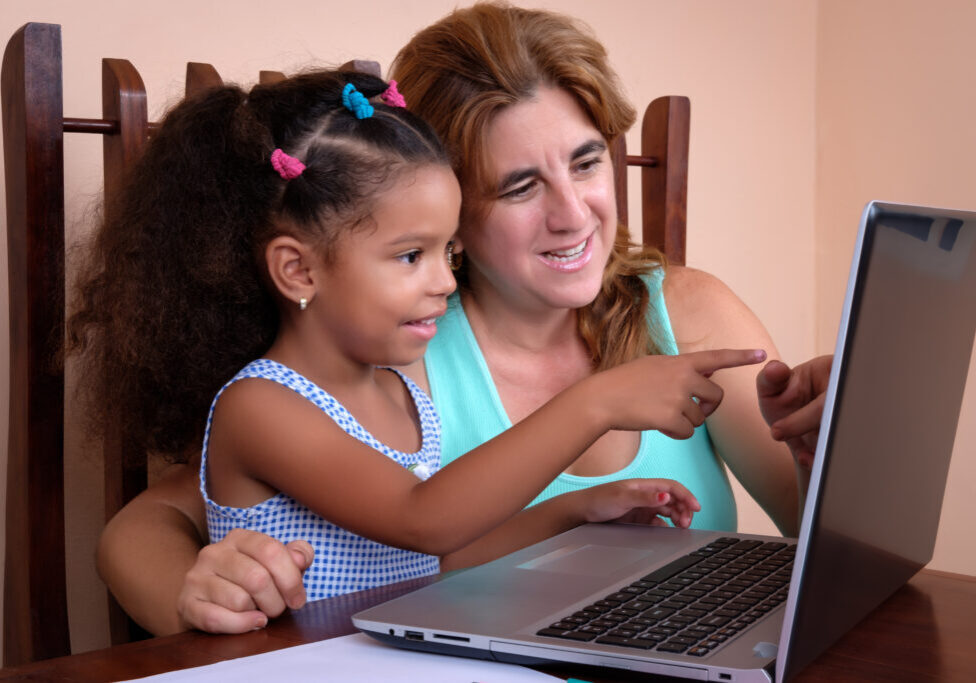 Cute multiracial small girl and her mother using a laptop computer at home